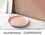 Small photo of Summer still life scene with empty blank pink plate, marble boards. Eco minimalist mockup with window shadow. Tableware set. Front diagonal view