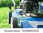 Small photo of Lawn mower cutting grass. Small grass cuttings fly out of lawnmower. Grass clippings get spewed out of a mower pushed around by landscaper. CloseUp. Gardener working with mower machine. Mowing lawns