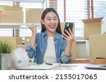Cheerful small business entrepreneur SME, happy asian young woman owner smile when receive order from customer on app shopping by smartphone, mobile. Merchant online, ecommerce working at home office.