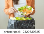 Small photo of Compost from leftover food, asian young housekeeper woman hand holding cutting board use fork scraping waste, rotten vegetable throwing away into garbage, trash or bin. Environmentally responsible.