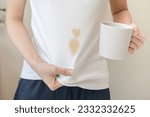 Small photo of Cloth stain, disappointment asian young woman clumsy with hot coffee, tea stains on shirt, hand show making spill drop on white t-shirt, spot dirty or smudge on clothes at home, isolated on background
