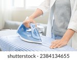 Small photo of Close up young woman hand use electric steam, hot iron press pile stripe shirt clothes on ironing board, housework after hygiene laundry at home. Housekeeping lifestyle, household of chores concept.