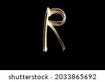 Letter R. Light painting alphabet. Long exposure photography. Drawn letter R with gold lights against black background.