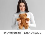 Young woman studio standing isolated on gray wall holding teddy bear looking camera smiling friendly