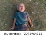 Small photo of a little boy lies on the ground and cries a lot. resentment or hysteria in a child.