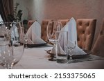 Small photo of proper serving in restaurant. table covered with a white tablecloth, cutlery and glasses on the table. soft beige chairs. premium restaurant. serving cutlery according to the rules of etiquette.