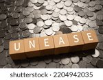 Small photo of Wooden blocks with "UNEASE" text of concept and coins.