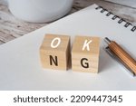 Wooden blocks with "OK NG" text of concept, a pen, a sketchbook, and a cup.