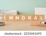 Small photo of Wooden blocks with "IMMORAL" text of concept, pens, notebooks, and books.