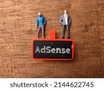 Wooden board and miniature people with text AdSense on a wooden background.