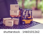 Logistics, supply chain and delivery service concept : Fork-lift truck moves a pallet with box carton. Boxes on a laptop computer, depicts wide spread of products around globe in ecommerce booming era
