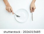 Women's hand ,White empty plate and hand holding silver fork and spoon on white background, top view, copy space
