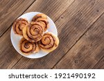 Cinnabon buns. Freshly baked cinnamon roll with spices and cocoa filling and coffee or cappuccino on white serving plate on wooden background with copy space. Swedish breakfast.