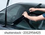 Male auto specialist worker hand rolling car window film on front windscreen glass surface. Car side window film removal and tinting installation. 