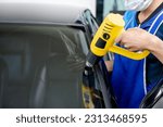 Small photo of Auto specialist worker hand blowing hot air dryer or hairdryer removing old car window film tint and installing the new one. Car front windscreen film removal and tinting installation
