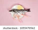 Small photo of A bass fish with arms and legs of a doll inside on a flower plate. Cannibalism and anthropomorphism on a pink feminine background. quirky minimal color still life photography.