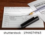 Small photo of Close up isolated image of a COVID 19 vaccination record card on a wooden desk. The card details the date, type and the dose number of administered vaccine and given to every person for record.