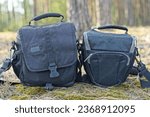 two different black colors, stylish, closed with a zipper, fashionable made from nylon, modern soft, professional with comfortable handles, camera bags stand on the ground in the forest during the day