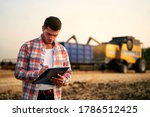 Small photo of Farmer controls loading wheat from harvester to grain truck. Driver holding clipboard, keeping notes, cargo counting. Forwarder fills in consignment waybills. Agricultural commodities logistics.