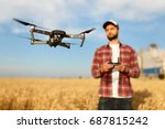 Compact drone hovers in front of farmer with remote controller in his hands. Quad copter flies near pilot. Agronomist taking aerial photos and videos in a wheat field. Innovations in agriculture