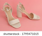 One pair of white women's sandals with high and square heels stands on a pink paper background, close-up side view.