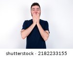 Small photo of Vivacious Young caucasian man wearing black T-shirt over white background , giggles joyfully, covers mouth, has natural laughter, hears positive story or funny anecdote