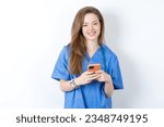 Small photo of Young caucasian doctor woman wearing medical uniform enjoys distant communication, uses mobile phone, surfs fast unlimited internet, has pleasant smile, makes shopping online