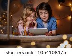 Small photo of Children keen on watching cartoons. Boy holding tablet in hands and girl propping up head with hands. They are lying on the floor in snuggery nursery.