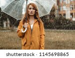 Waist up portrait of unhappy girl holding umbrella in hands. She is looking at camera with discontent 