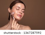 Relaxed young woman standing isolated on the brown background and smiling with closed eyes while using rose quartz face roller