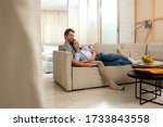 Happy husband and wife switching channels with remote control in living room at home