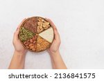 Female hands hold a plate divided into sectors with various seeds and nuts. Concept: vegetarian and vegan food. Natural nutrition