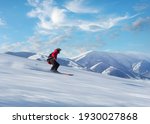 Happy person in red jacket skiing down slope in bright sunshine on blue sky, with high snow covered mountains in background. Blurred motion.