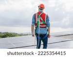 Construction worker wearing safety harness and safety line working on solar cell on roof factory.