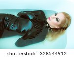 Hot dominant blonde mistress woman in wet shiny latex fetish dress, gloves and spiky leather collar posing in white bath with blue water