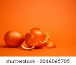 Small photo of One whole orange and one balloon inside of an orange peel isolated on a vibrant orange background. Abstract food composition, merging the incompatible. Creative fruit concept.