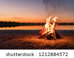 Small campfire with gentle flames beside a lake during a glowing sunset. Western Australia, Australia.