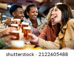 Small photo of Group of smiling friends drinking and toasting beer at bar restaurant - Friendship concept with young happy people having fun together toasting brew pint on happy hour