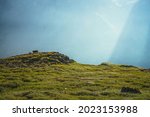 Colorful green landscape with rocks and hills on background of giant mountain wall in sunlight. Minimalist vivid sunny scenery with sun beams and solar flare. Minimal alpine view. Scenic minimalism.