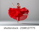 Small photo of young graceful ballerina, dressed in pointe shoes and a weightless red skirt, demonstrates her dancing skills. The beauty of classical ballet.