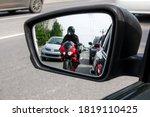 The side mirror of the car reflects a motorcyclist who is moving between cars very close to them