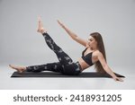 Small photo of Sportswoman with long fair hair doing crunches in studio. Side view of young Caucasian female raising arm and leg, while having abs workout, isolated on grey background. Concept of sporty lifestyle.