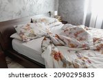 An Unmade Bed With Flowery...