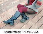 Female legs dressed in knee high boots and knitted stockings, woman sitting on a wooden planking, winter outdoor