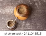 Small photo of Yerba Mate tea with a small wooden mate next to a gourd filled with yerba mate, on a light gray background.