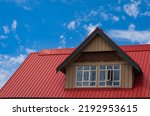 Red roof with dormer in the blue sky background. Decorative metal roof. Types of roof roofs.The roof of the house from a metal profile. Roofing. Stainless steel cladding. Nobody, copyspace for text