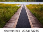 Small photo of Wooden pier on the forest lake. Swampland walkway wooden board path in Whonnock lake park. Nature park wooden walkway. BC parks. View of of the marsh and boardwalk. Wooden deck waterfront
