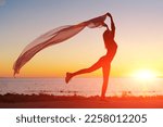 Silhouette slender girl at sunset on seashore rejoices with a transparent cloth in her hands in the wind. Emotional freedom concept
