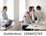 Small photo of Young woman meditating practicing yoga sitting at office sill avoiding colleagues looking at girl with ironical smile, mocking and making fun of weird coworker, jeering or bullying at work concept