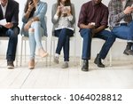 Diverse black and white people sitting in row using smartphones tablets, multiracial men and women waiting for job interview, human resources, employment or customers and electronic devices concept